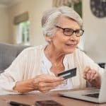 Smiling-senior-woman-paying-for-something-online-using-laptop-and-credit-card